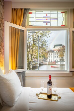 A hotel room with a bed, a window with curtains, a bottle of wine, and two glasses on a tray. - Hotel Oscar (Amsterdam)