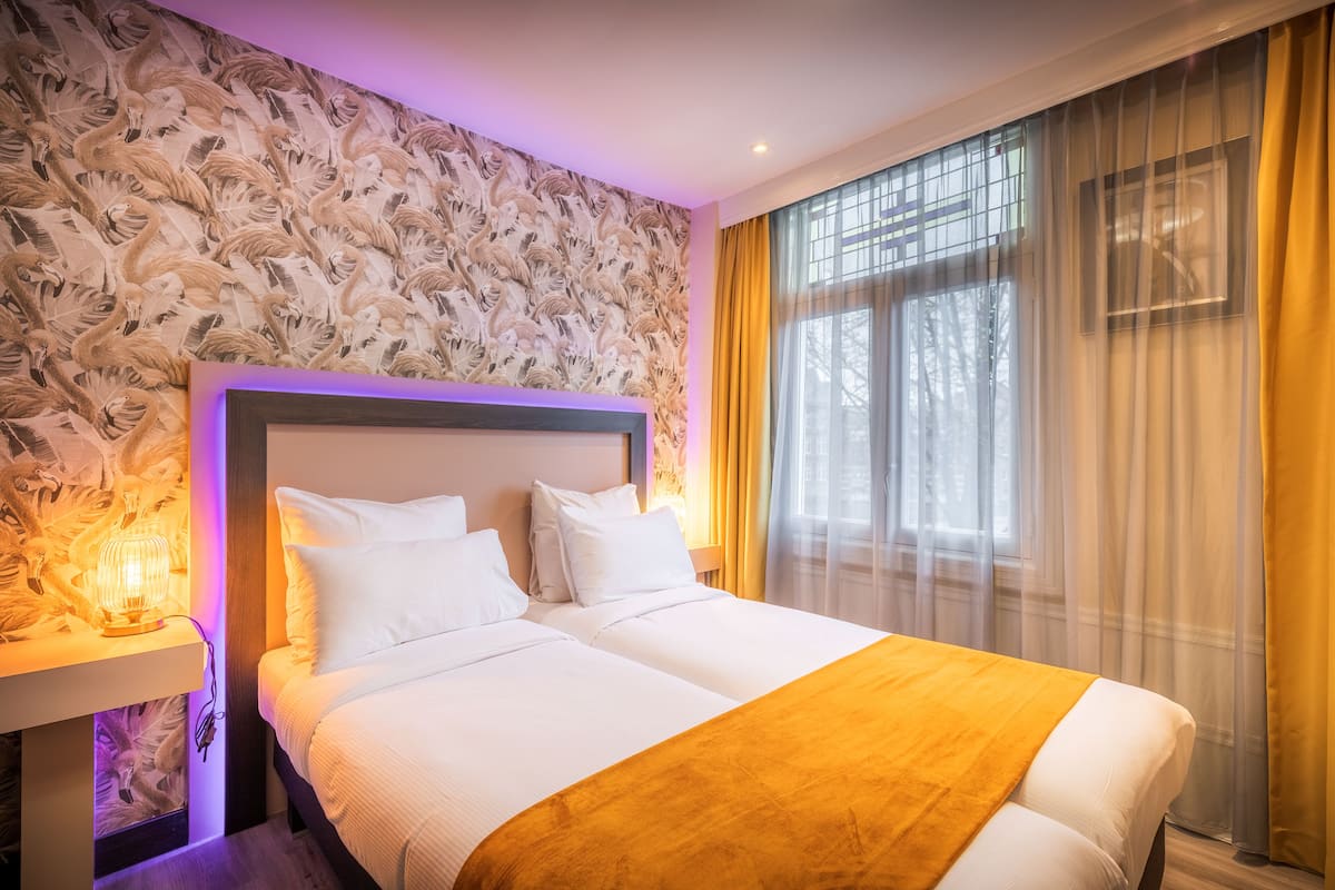 A hotel room with a large bed, a bedside table with a lamp, and a window with curtains.