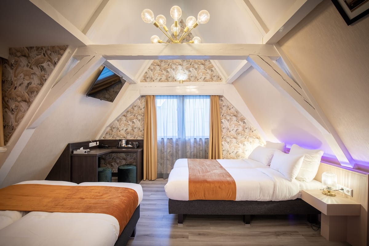 A cozy attic bedroom with two beds, a desk, and a chandelier.