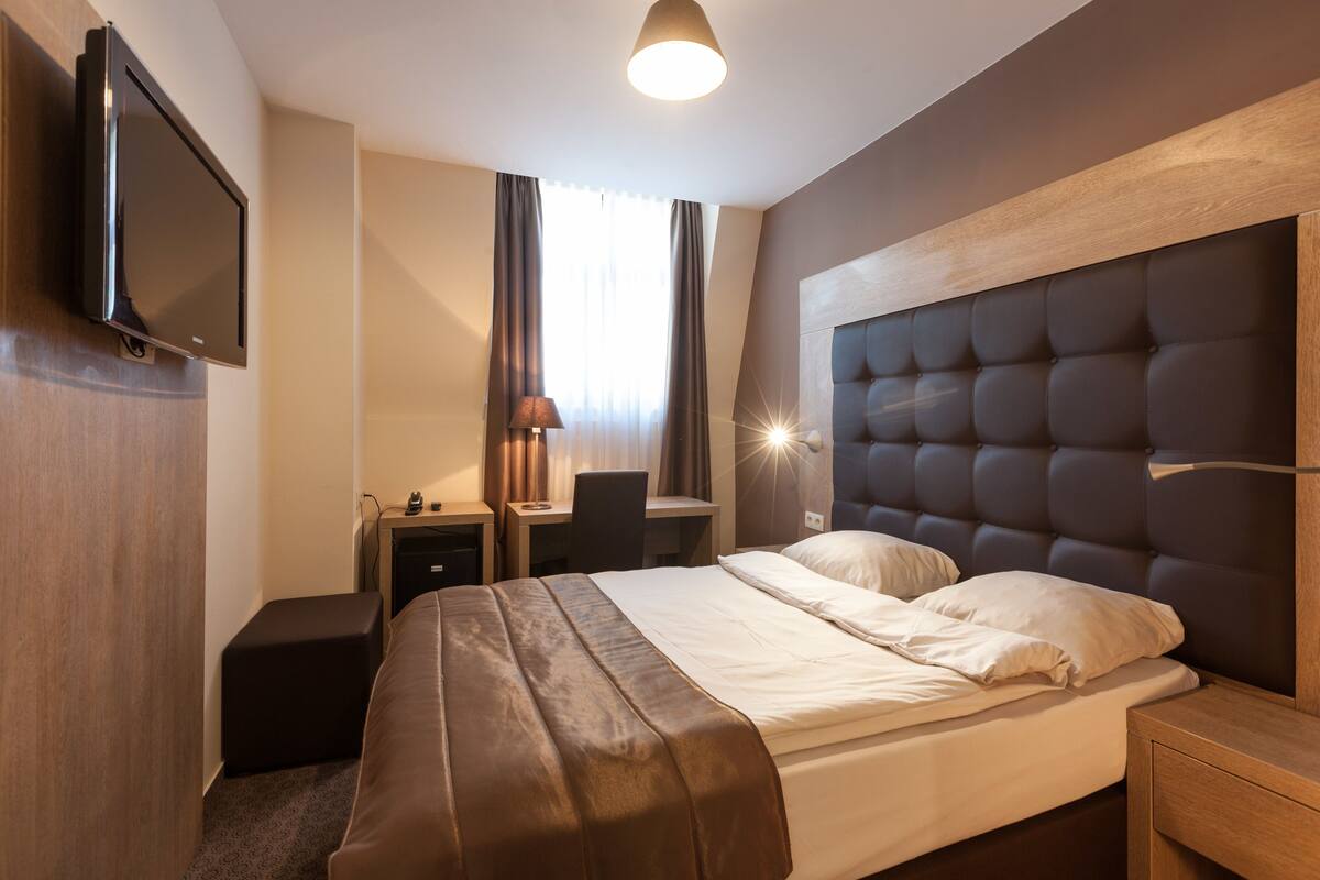 A hotel room with a bed, a desk, a chair, a TV, and a nightstand.