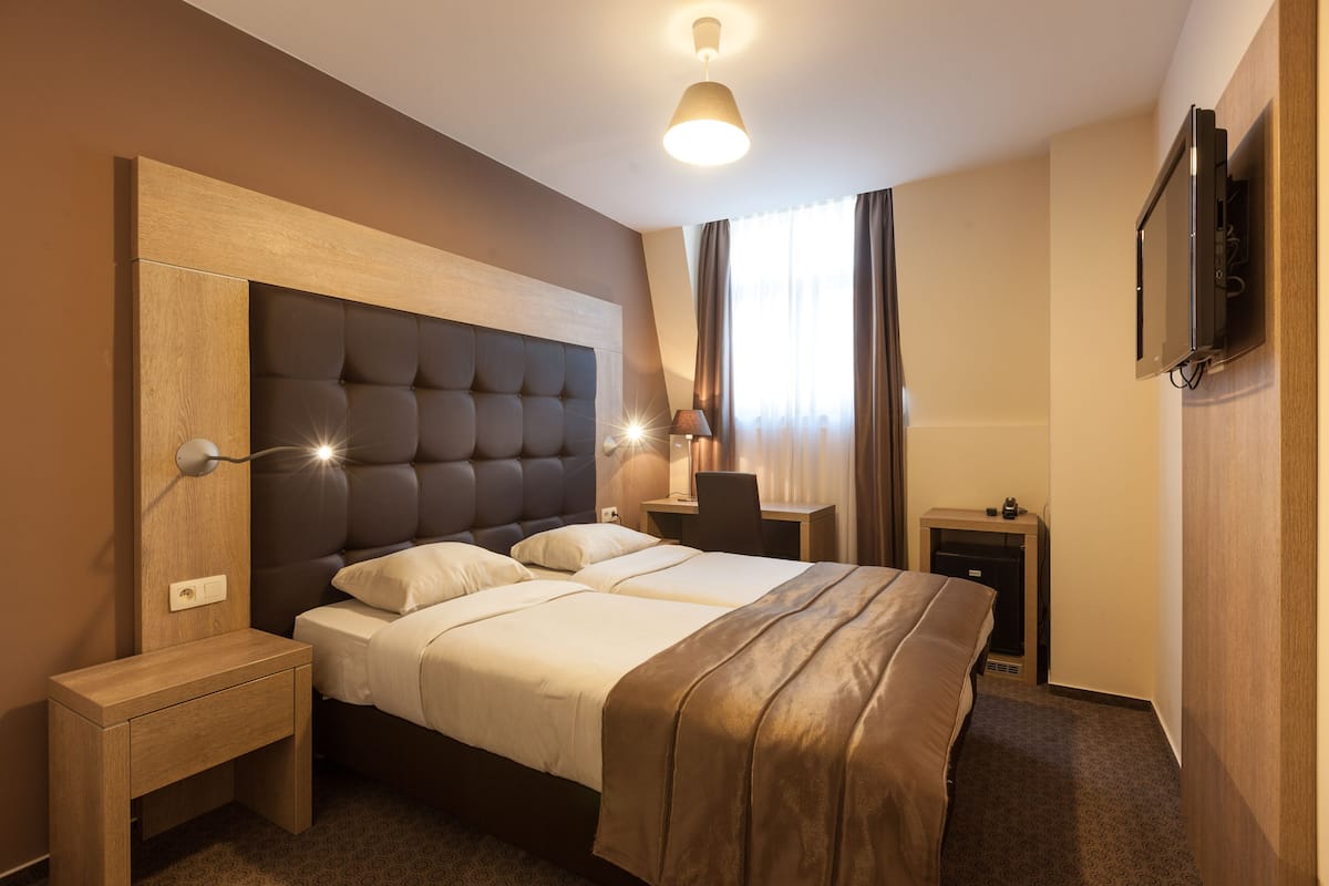 A hotel room with a large bed, bedside tables, a desk, a lamp, and a TV mounted on the wall.