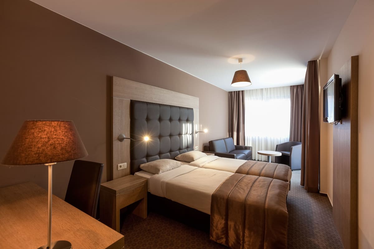 A hotel room with two beds, a desk, a chair, a TV, and a lamp.