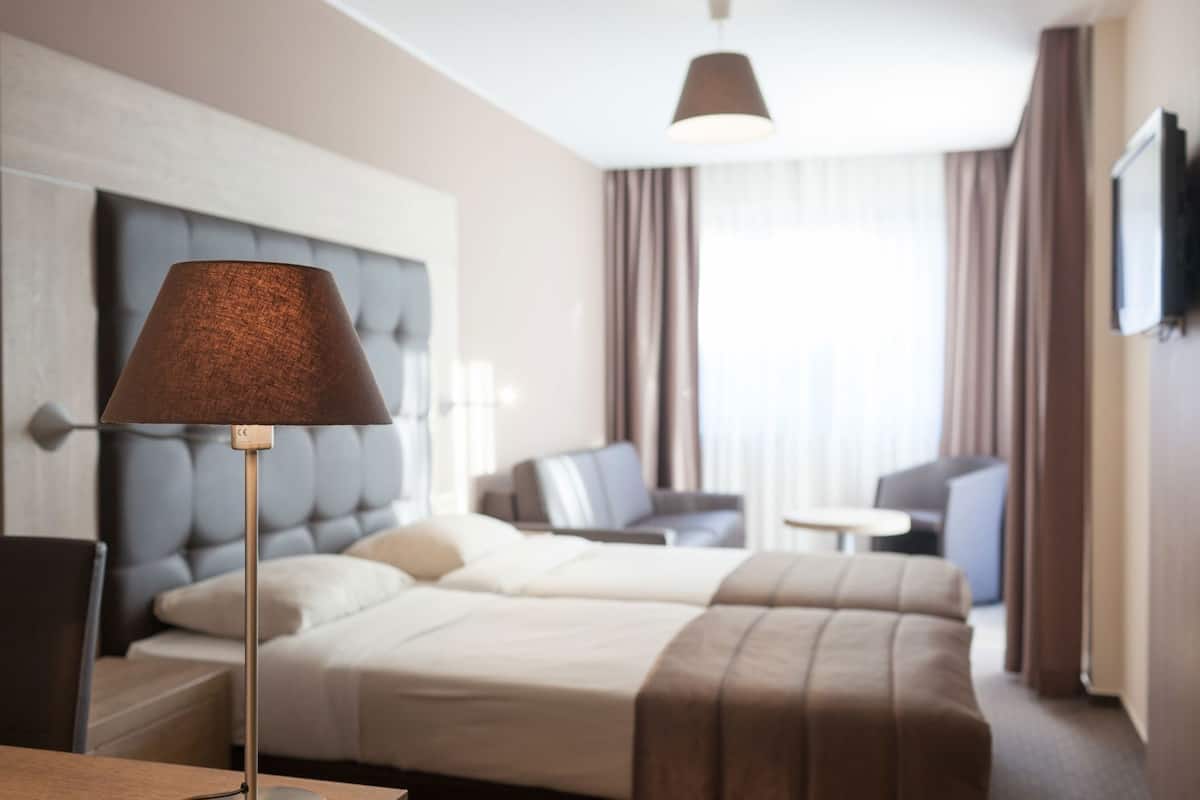 A hotel room with a bed, bedside tables, a lamp, a sofa, and a TV.