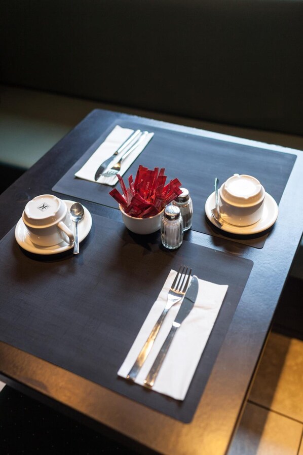 Una mesa de comedor elegantemente dispuesta, con platos blancos, cubiertos y un bol de servilletas rojas.
