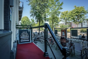 A hotel entrance with a red carpet, a sign for the hotel library, and bicycles parked outside.