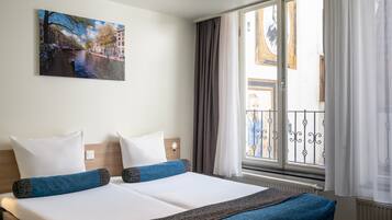 A hotel room with a bed, a painting of a canal, a window with curtains, and a view of a building.