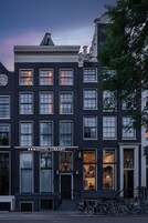 Un immeuble à plusieurs étages, reconnaissable à son panneau bien visible indiquant « HÔTEL – BIBLIOTHÈQUE », à ses grandes fenêtres et à une rangée de vélos garés à l’extérieur.
