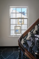 Un escalier avec une rampe en bois et une fenêtre ornée d’œuvres d’art encadrées.
