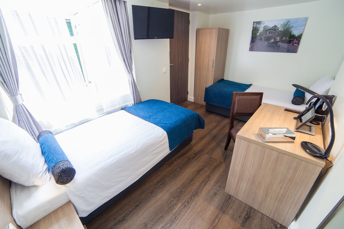 A hotel room with two beds, a desk, a chair, a TV, and a painting on the wall.