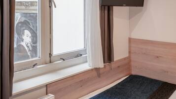 A room with a bed, a window with curtains, a radiator, and a mounted television.