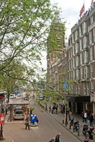 Une vue de rue avec un immeuble doté d’une tour, des voitures garées et des piétons.