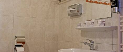 Un baño con lavamanos, espejo, dispensador de toallas y soporte para papel higiénico.