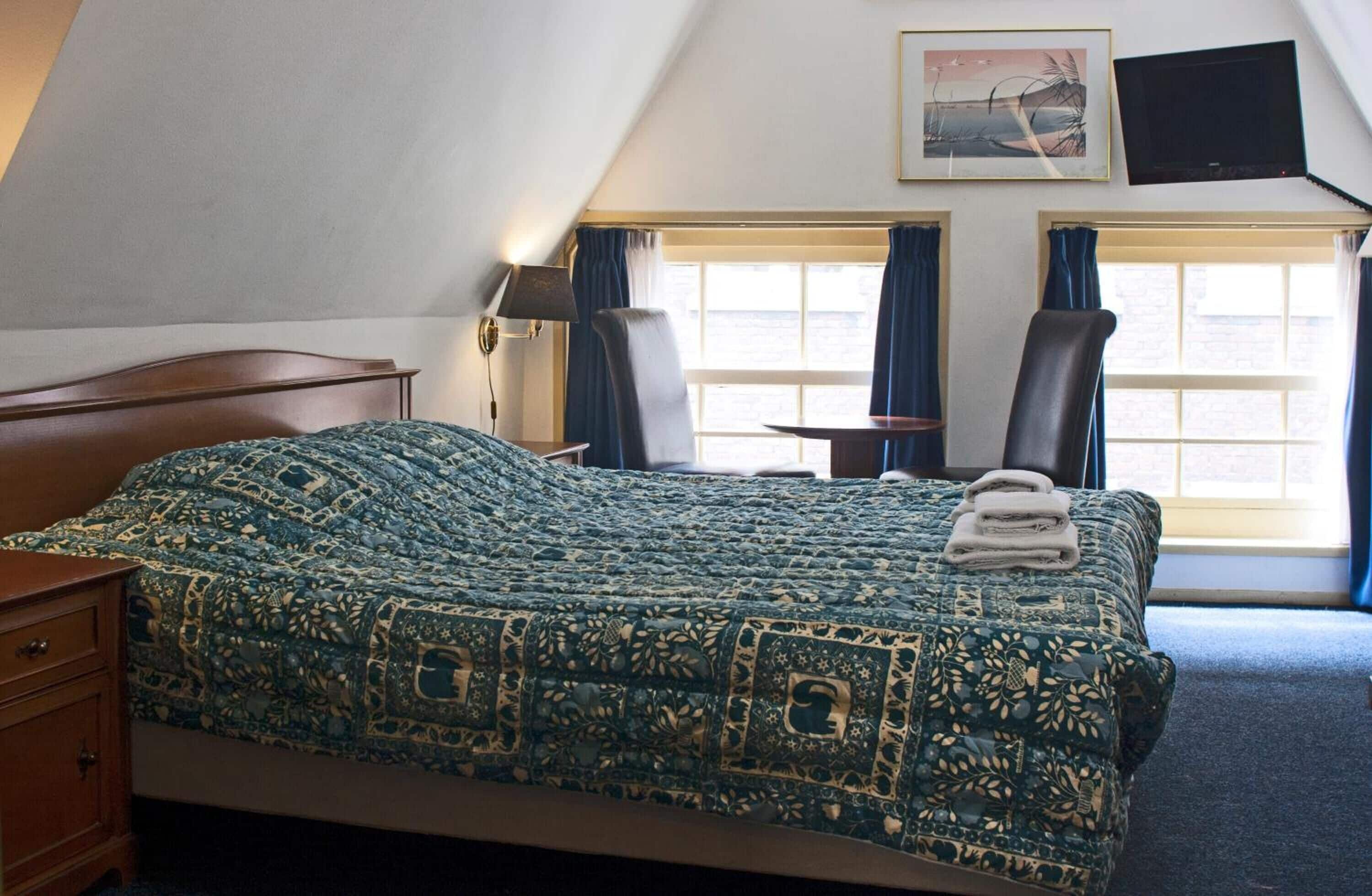 Una habitación de hotel con una cama grande, dos sillas, un escritorio, un televisor y una ventana con cortinas.
