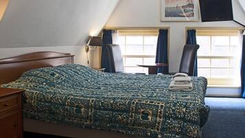 Una habitación de hotel con una cama grande, dos sillas, un escritorio, un televisor y una ventana con cortinas.