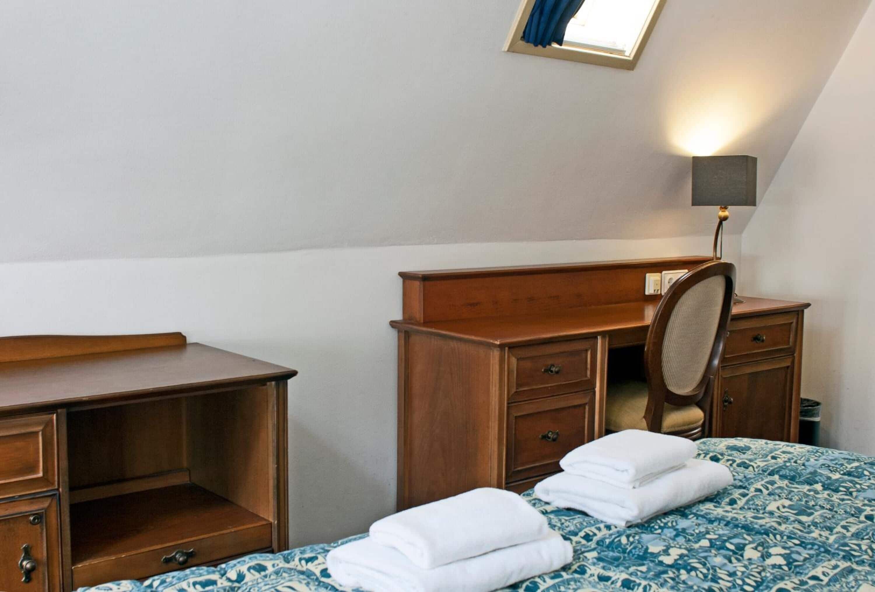 A bedroom with a bed, a wooden dresser, a mirror, and a desk.