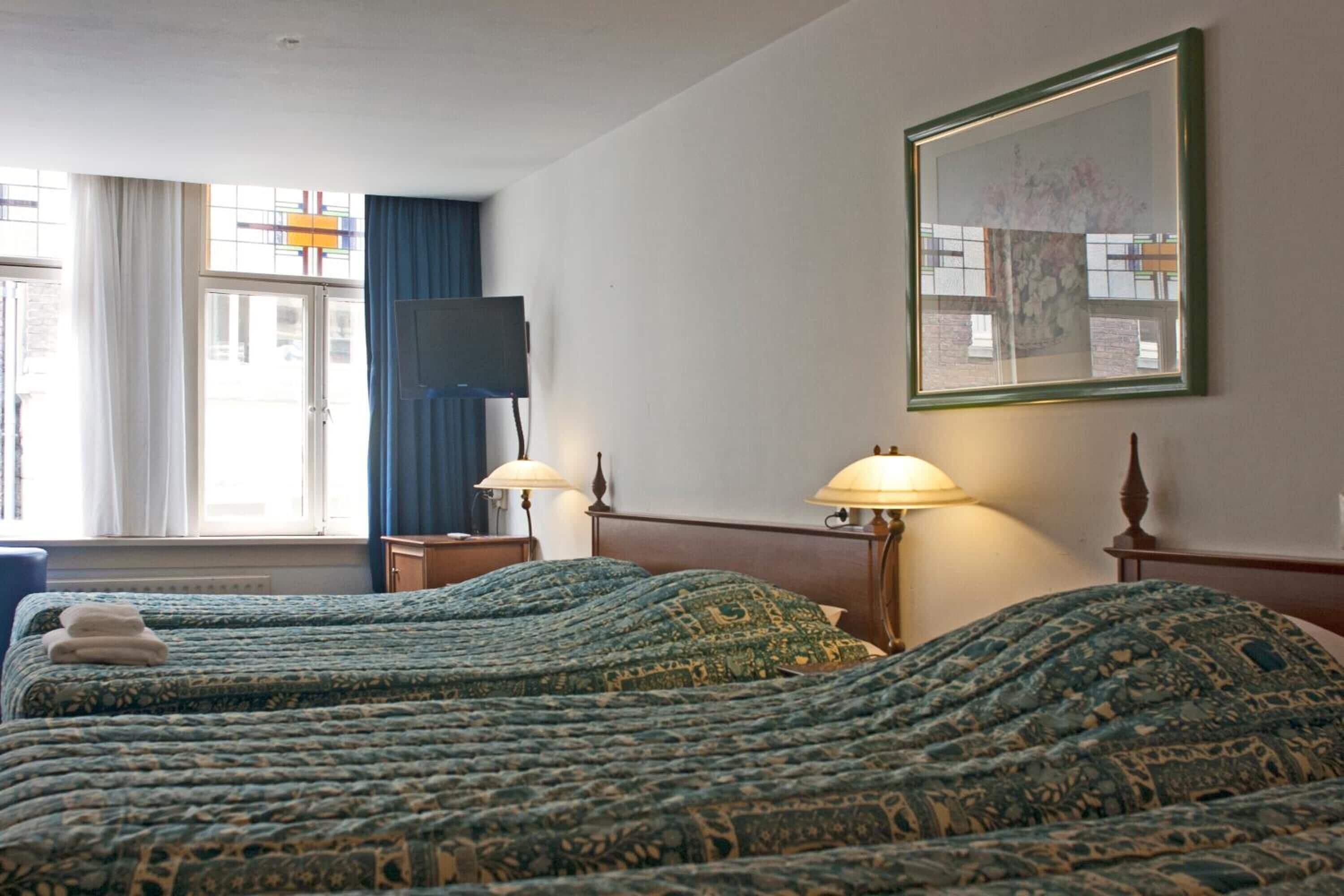 A hotel room with two beds, a television, a framed picture on the wall, and a window with curtains.