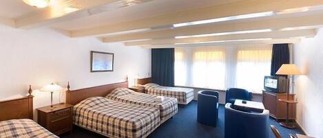 A hotel room with two beds, a desk, a chair, a TV, and a window with curtains.