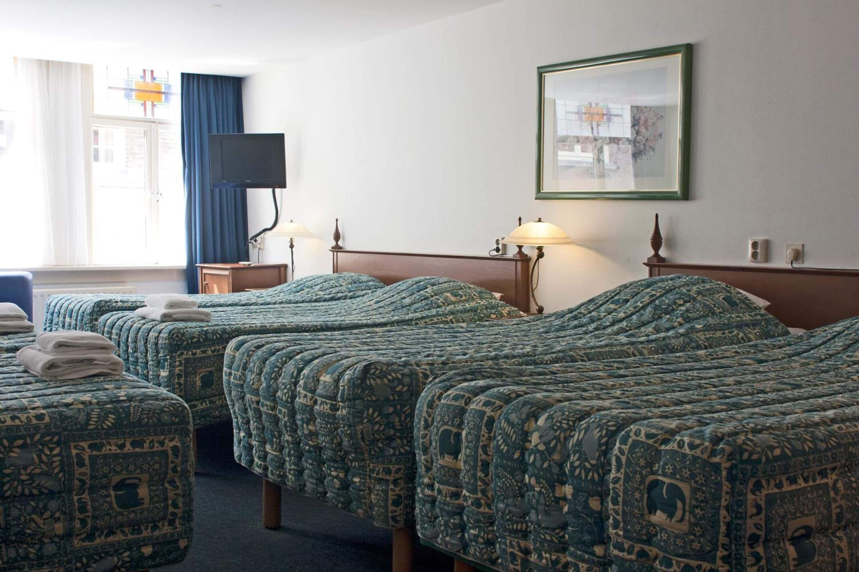 A hotel room with three beds, a television, a framed picture, and a window with curtains.