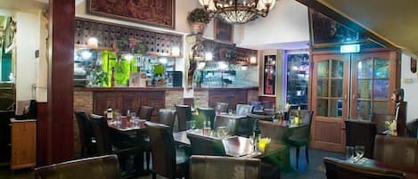 Interior de restaurante con mobiliario de madera, una zona de bar y una araña.