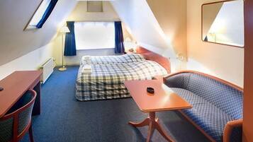 A small, triangular room with a bed, a sofa, a table, and a mirror.