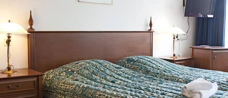 Habitación de hotel con una cama grande, dos mesitas de noche con lámparas, un televisor en la pared y un cuadro enmarcado sobre la cama.
