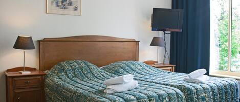 A hotel room with a large bed, two bedside tables, a TV, and a window with curtains.
