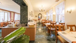 Un comedor de hotel con suelo de mármol, mesas y sillas de madera, una zona de bar central y candelabros.