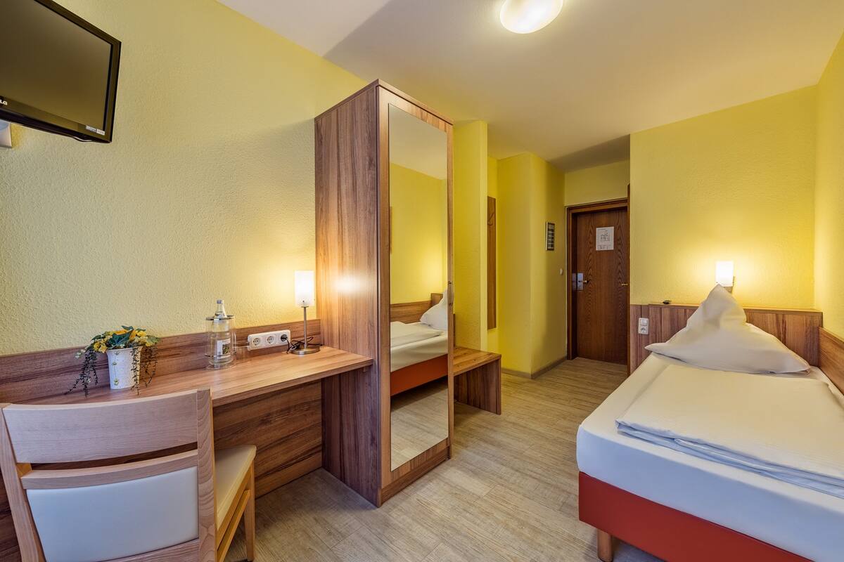 Ein Hotelzimmer mit Holzschreibtisch, Bett, Spiegel und Nachttisch mit Lampe.