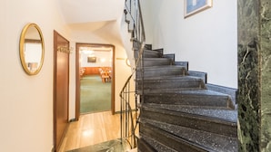 Una escalera con barandilla negra y escalones de mármol que conduce a una habitación con alfombra verde y muebles de madera.