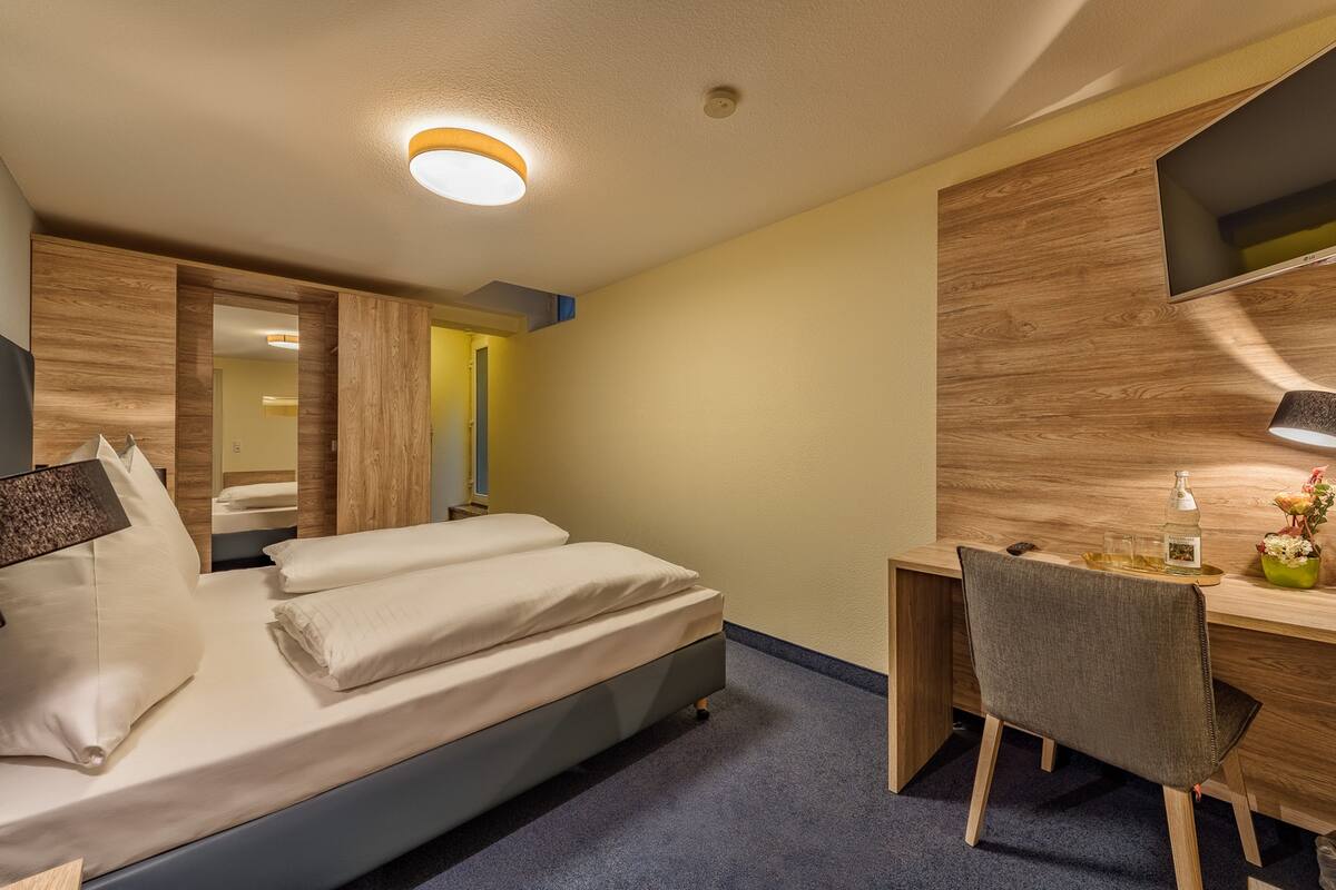 Ein modernes Hotelzimmer mit Bett, Schreibtisch, Stuhl und einem wandmontierten Flachbildfernseher.