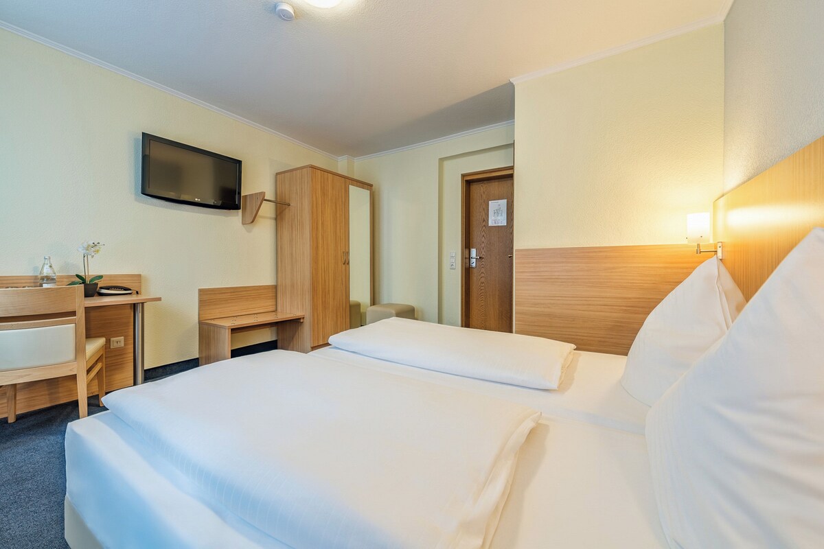 Habitación de hotel con dos camas, un escritorio, una silla, un televisor y un armario.