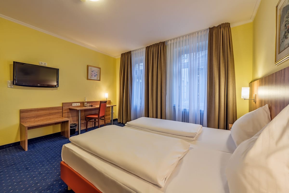 Ein Hotelzimmer mit Bett, Schreibtisch, Stuhl, Fernseher und einem Fenster mit Vorhängen.