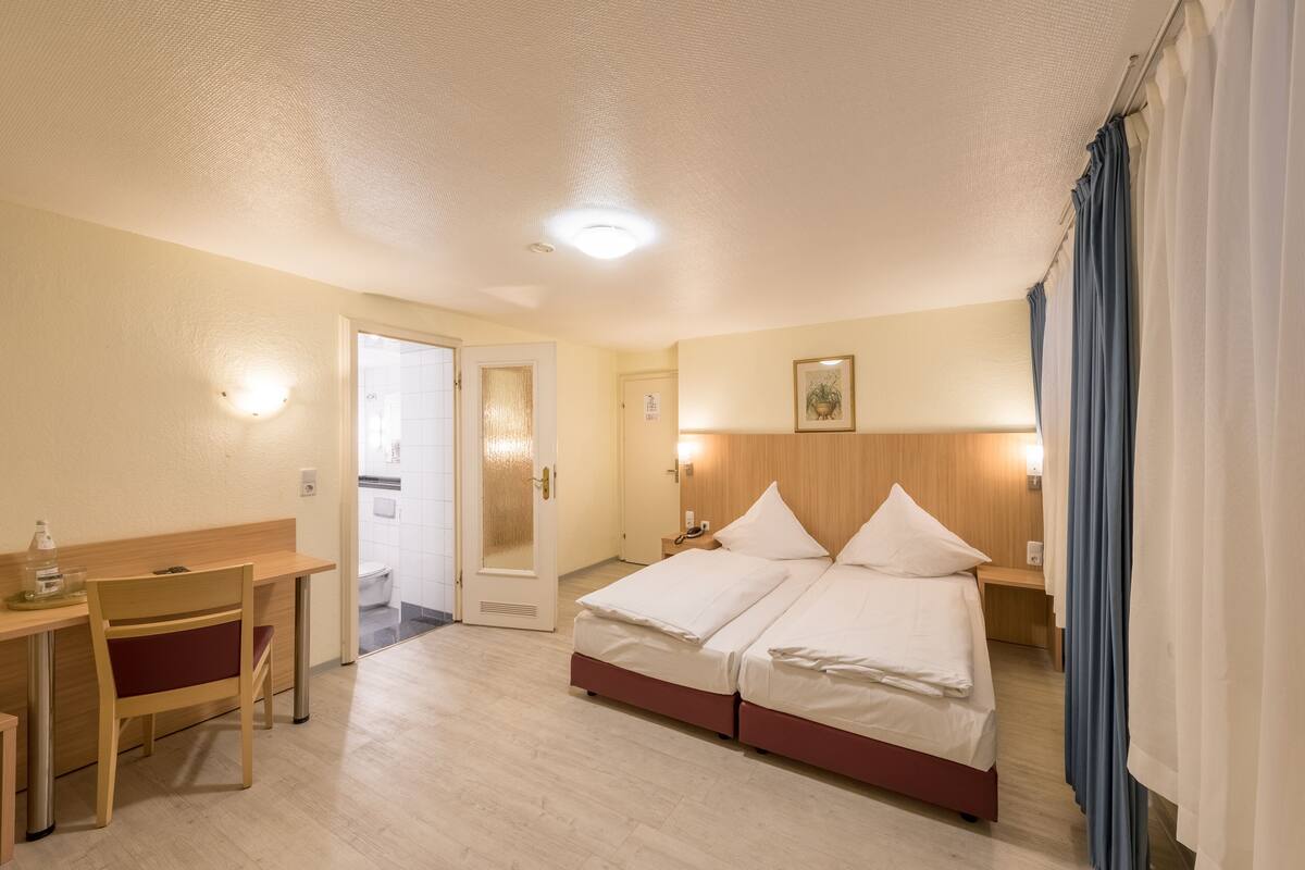 Ein Hotelzimmer mit einem Holztisch, einem Bett mit zwei Kissen, einem Nachttisch und einer Wandleuchte.