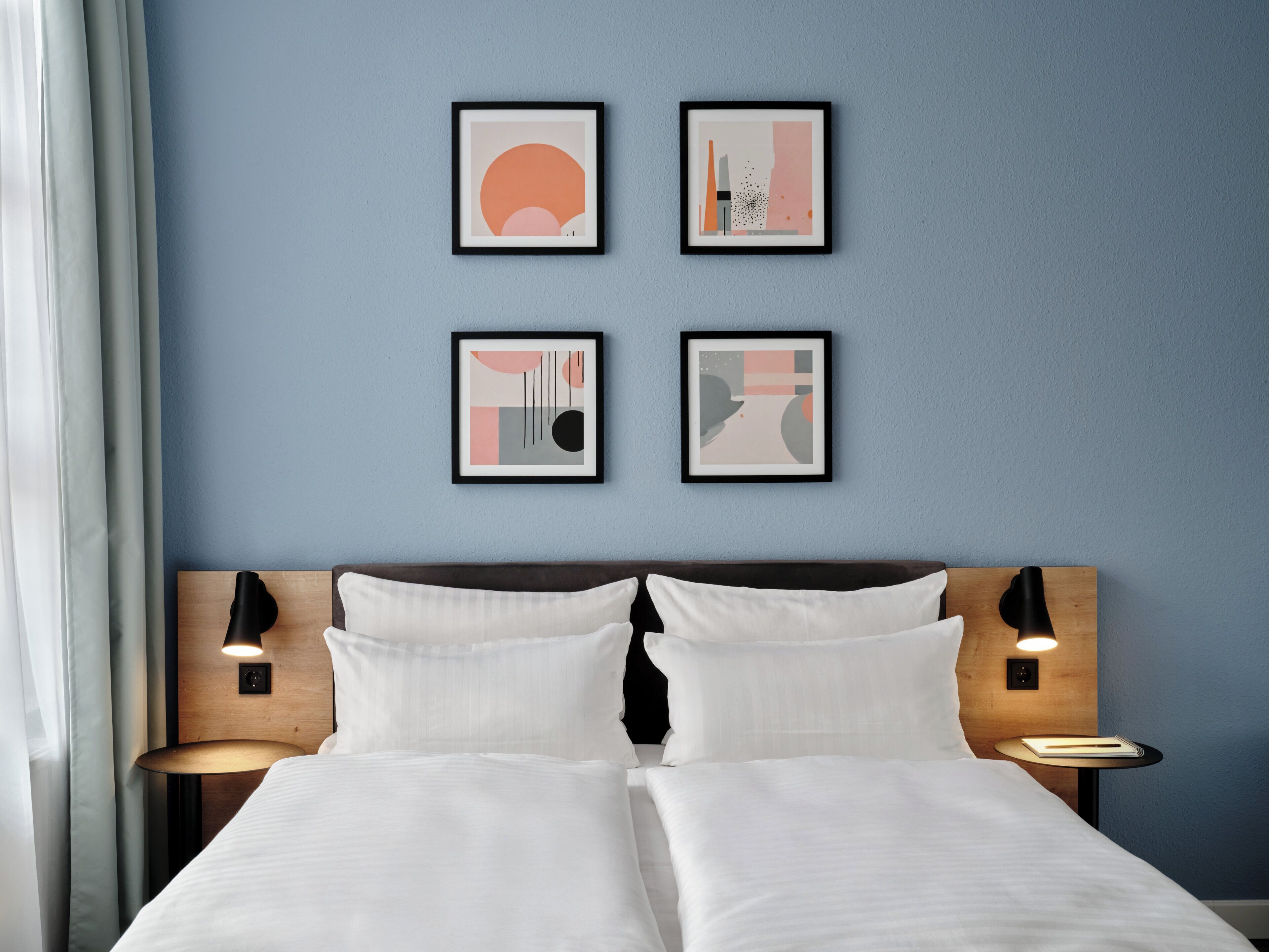 A hotel room with a bed, two bedside tables, and four framed artworks on the wall.