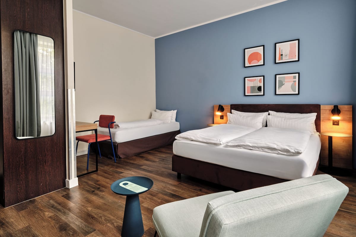 Habitación de hotel con dos camas, un escritorio, una silla y una mesita.
