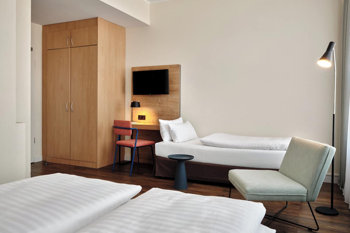 Habitación de hotel con dos camas, un escritorio, una silla, un televisor y una lámpara.
