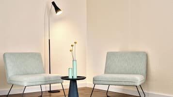A room with two light grey upholstered chairs, a small round table with a blue base, and a tall floor lamp with a black shade.