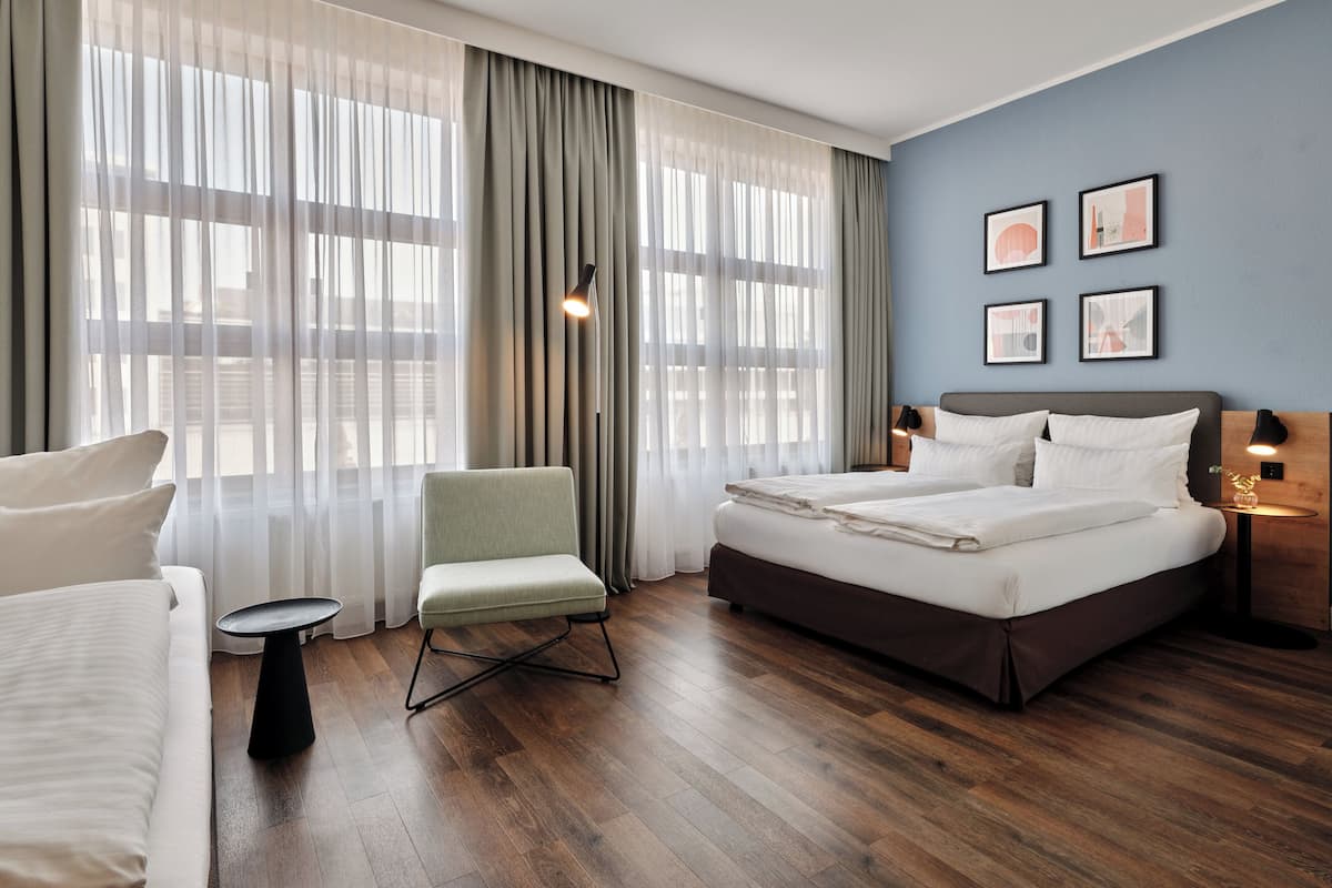Una habitación de hotel moderna con una cama grande, una zona de estar con una silla, una mesita y un escritorio con una lámpara.