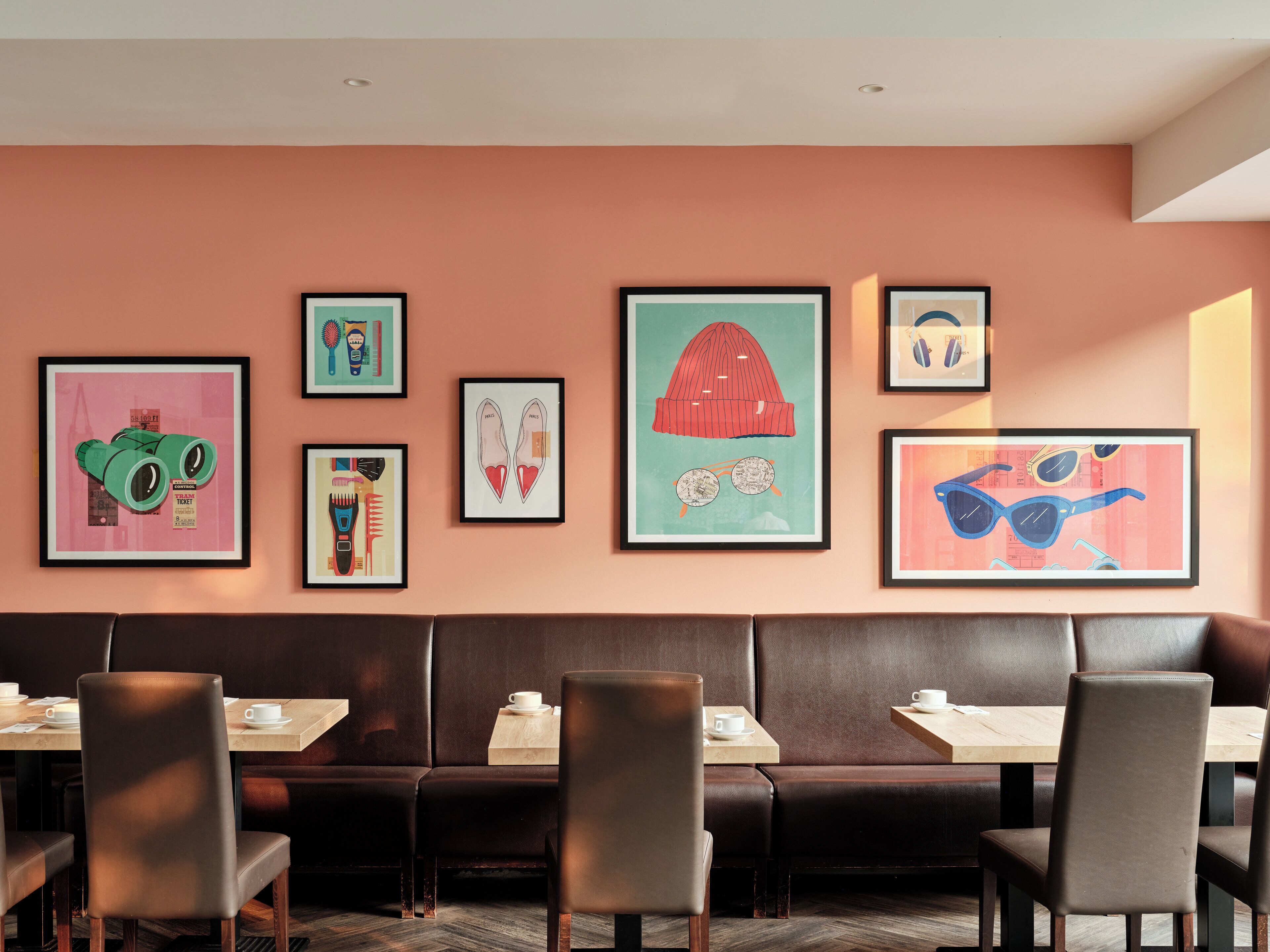 A restaurant with a long brown leather booth, several framed artworks on the wall, and a wooden table with a cup and saucer.