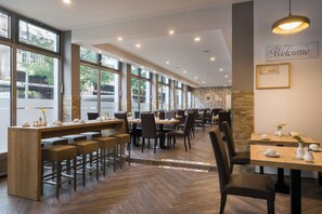 A modern restaurant with large windows, wooden tables, and bar stools. - Garner Hotel Berlin - Schöneberg by IHG (Berlin)