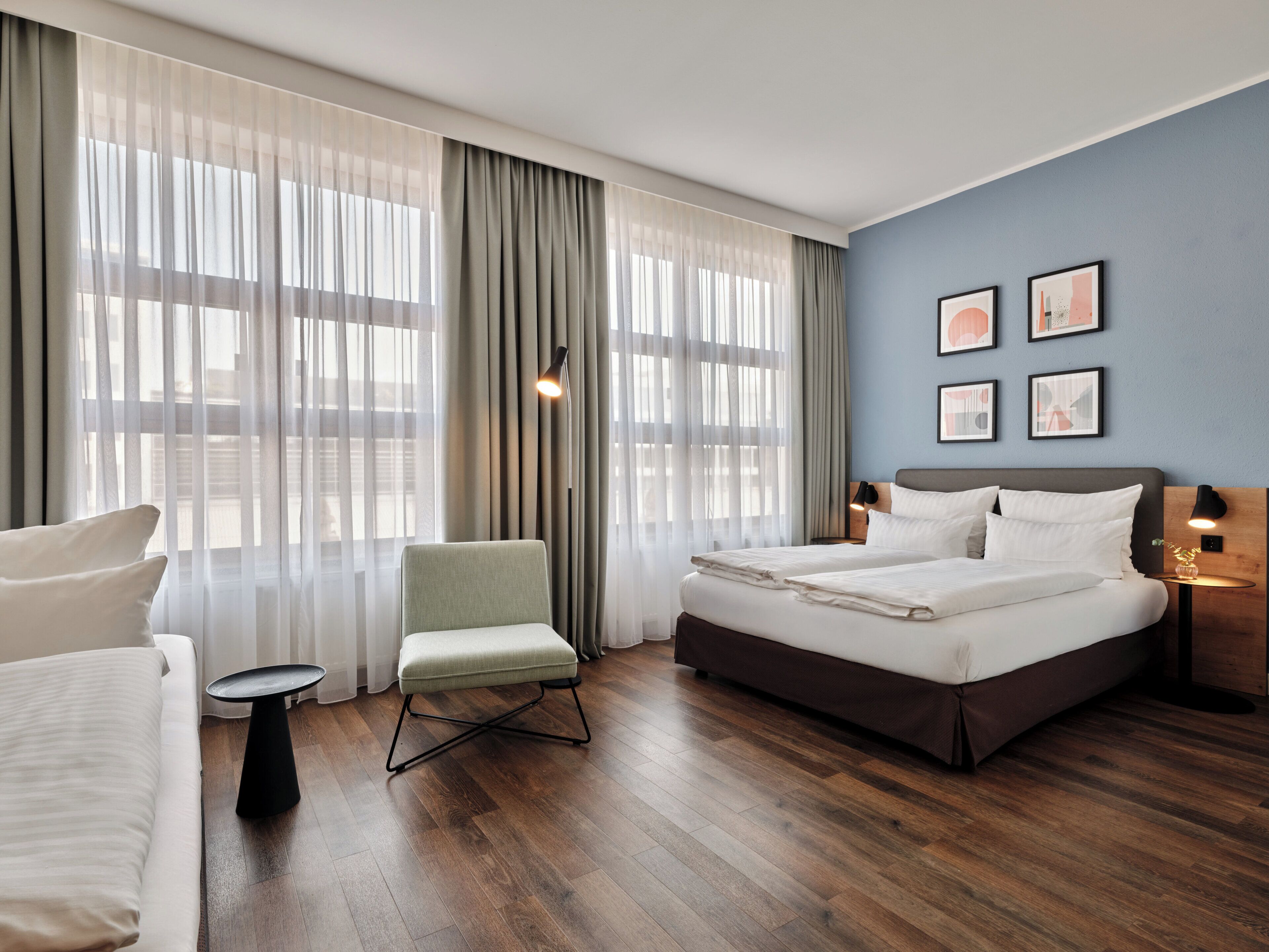 Una habitación de hotel moderna con una cama grande, una zona de estar con una silla, una mesita y un escritorio con una lámpara.