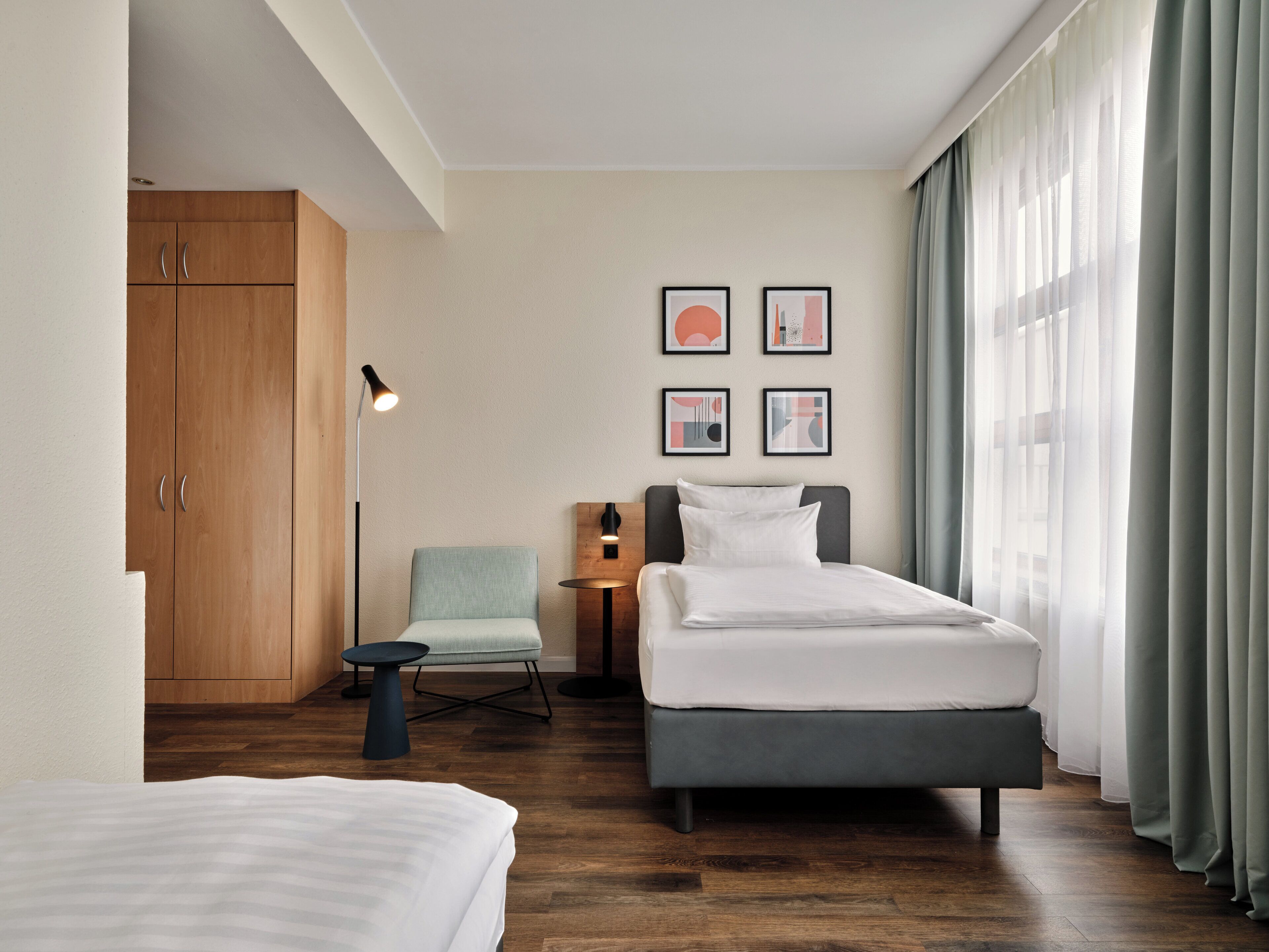 A hotel room with a bed, a chair, a desk, and a wardrobe.