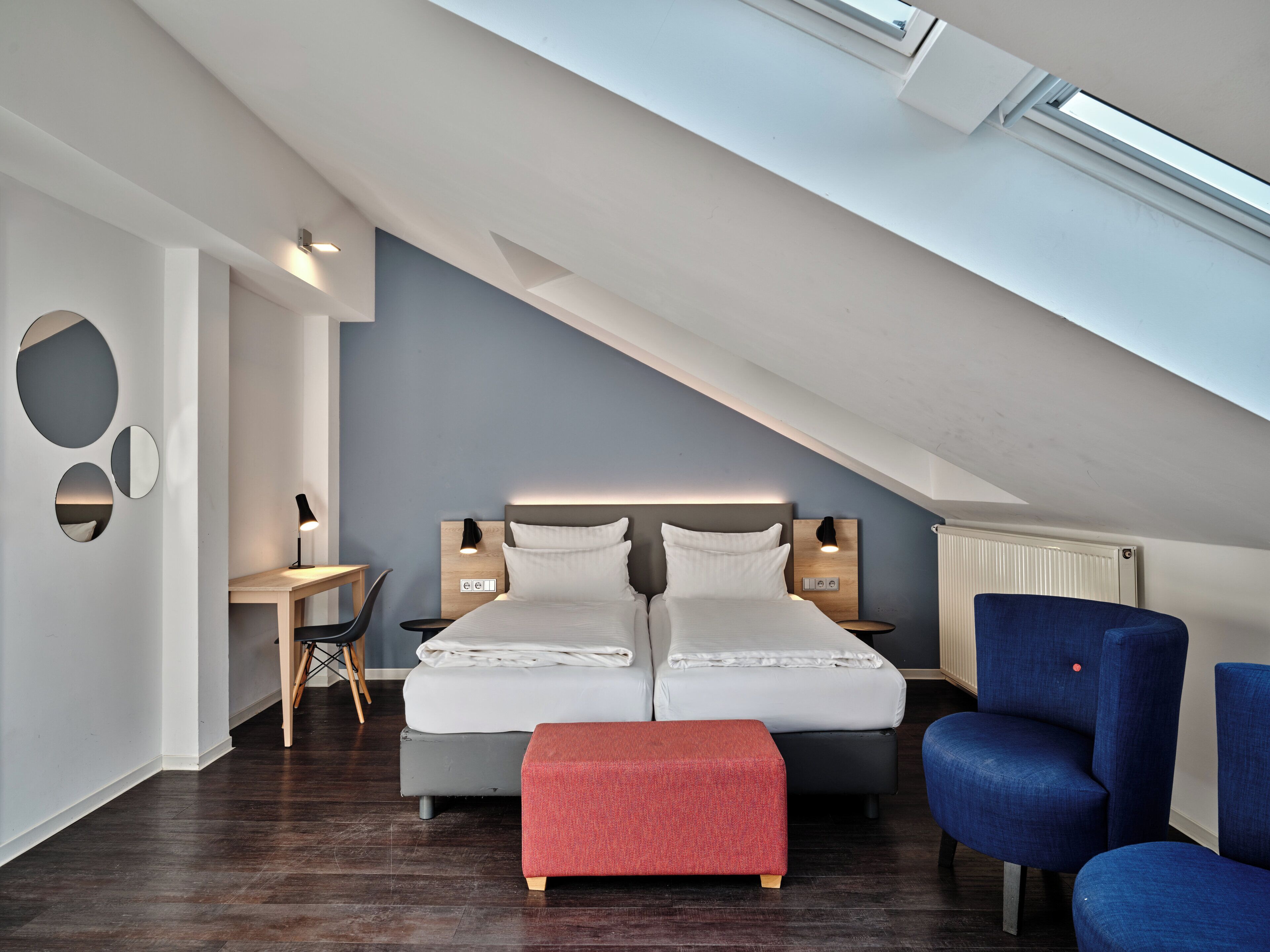 A modern bedroom with a sloped ceiling, a large bed, a desk, and a chair.