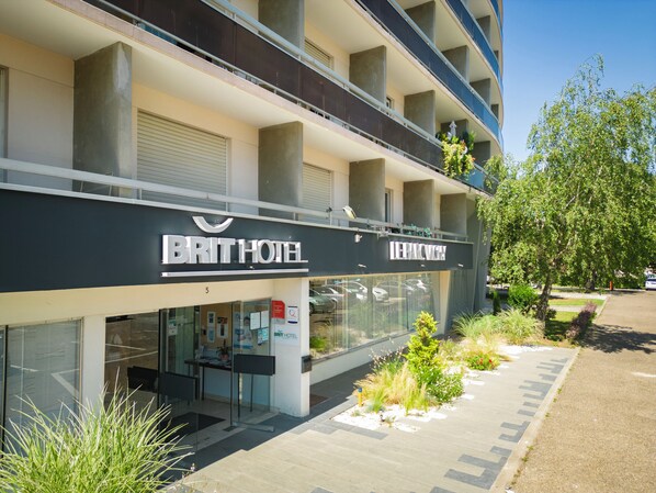 A modern hotel with a glass facade, outdoor seating, and a landscaped garden area.