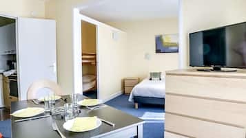 Habitación de hotel con una mesa de comedor preparada para dos personas, una cama con televisor, un aparador de madera y un armario con espejo.