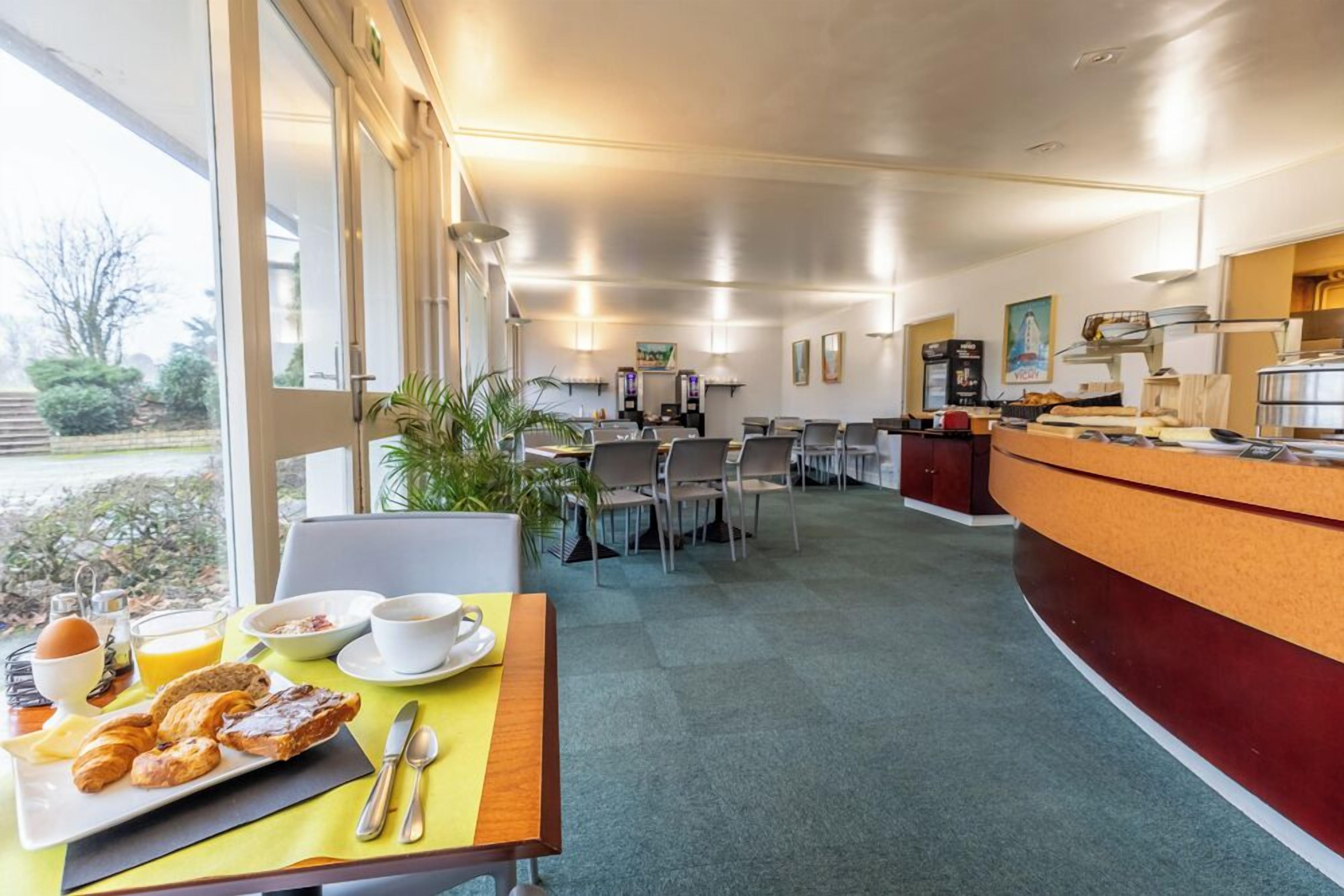 Un espace de restauration d’hôtel avec un buffet, des tables et des chaises, et une vue sur l’extérieur.