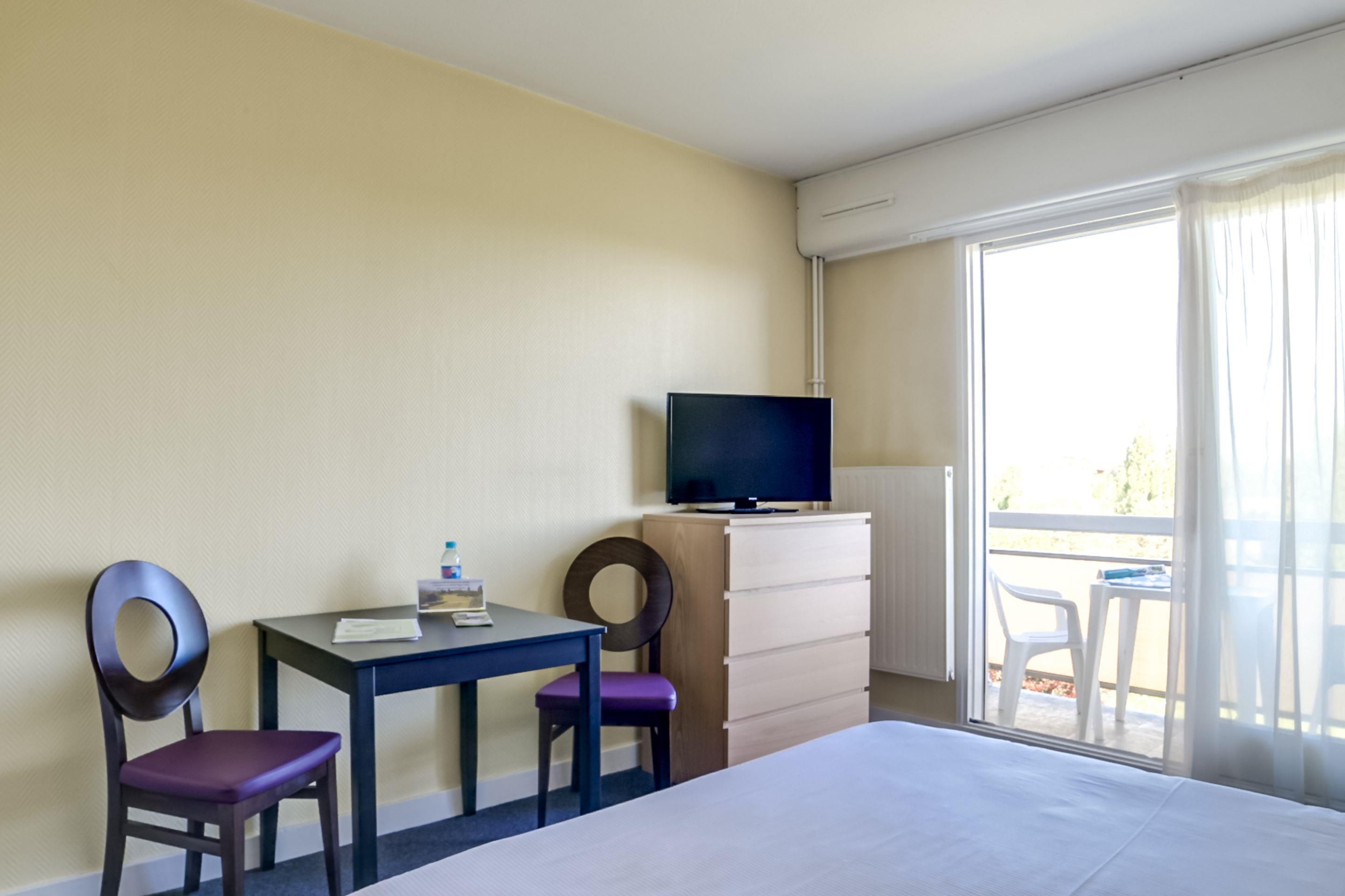 A hotel room with a bed, a desk with a chair, a television, and a view of the outdoors.