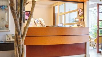 A reception desk with a wooden finish, a glass window, and a plant in the foreground.