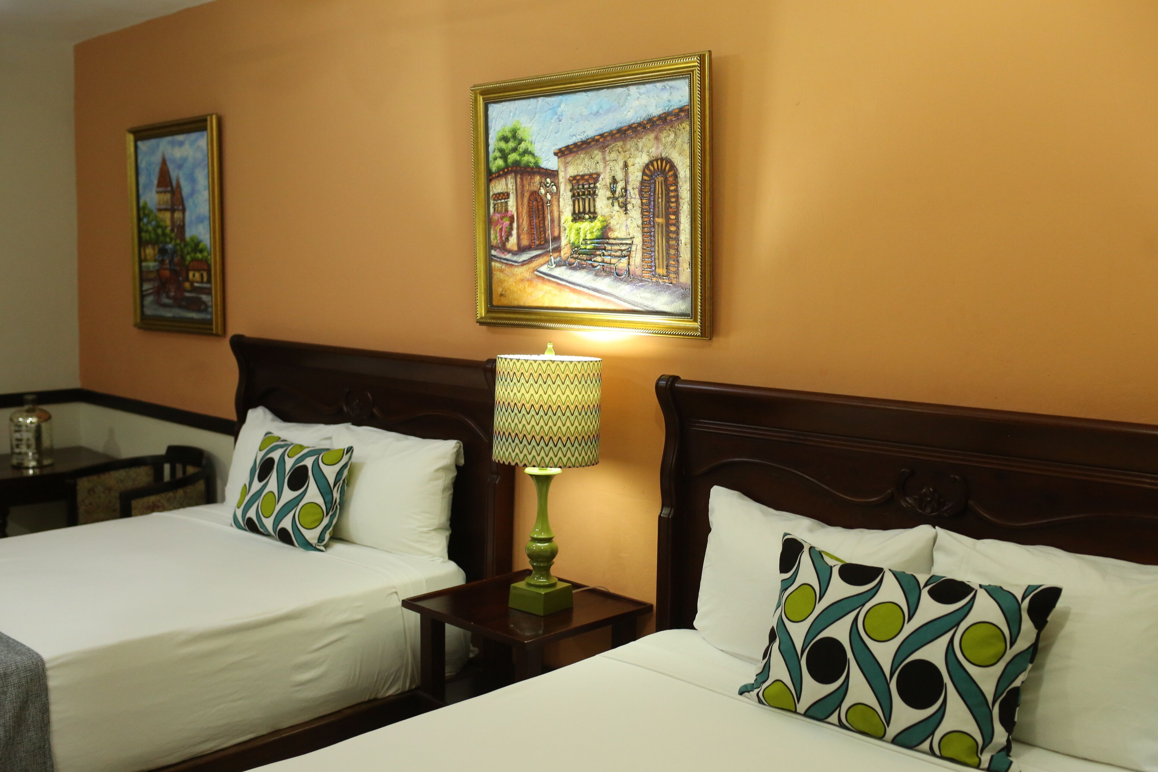 A hotel room with two beds, a nightstand with a lamp, and two framed pictures on the wall.