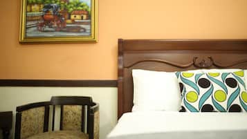 A hotel room with a wooden headboard, a bed with a patterned pillow, a chair, and a painting on the wall.